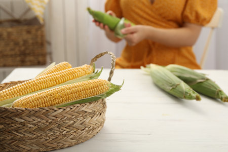 Woman husking corn cob at white wooden table, focus on basketの写真素材