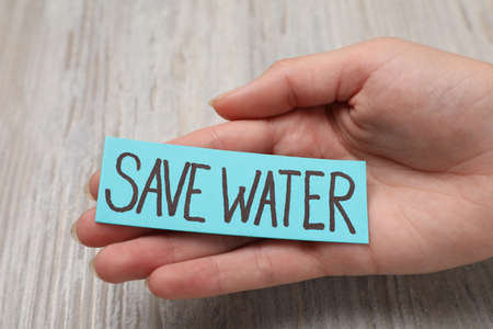 Woman holding card with words Save Water on wooden background, closeupの写真素材