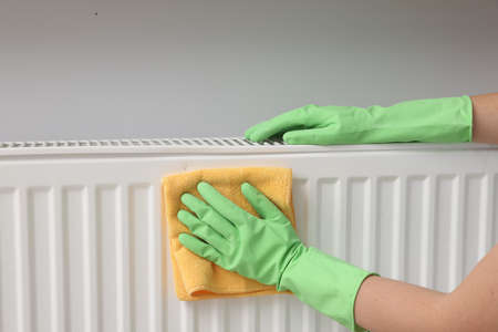 Woman cleaning radiator with rag indoors, closeupの写真素材