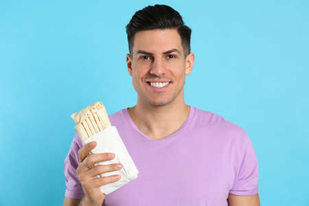 Man with delicious shawarma on turquoise background