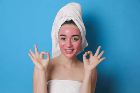 Woman with pomegranate face mask showing Ok on light blue backgroundの写真素材