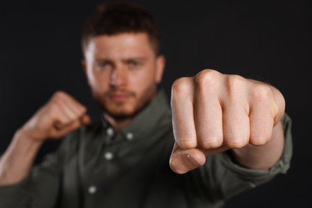 Young man ready to fight against black background, focus on hand. Space for textの写真素材