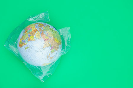 Globe in plastic bag and space for text on light green background, top view. environmental...