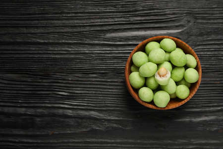 Tasty wasabi coated peanuts in bowl on black wooden table, top view. Space for textの写真素材
