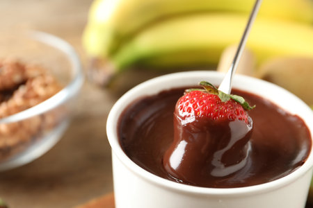 Dipping strawberry into fondue pot with chocolate, closeupの写真素材