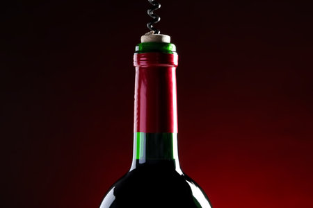 Opening wine bottle with corkscrew on dark red background, closeupの写真素材