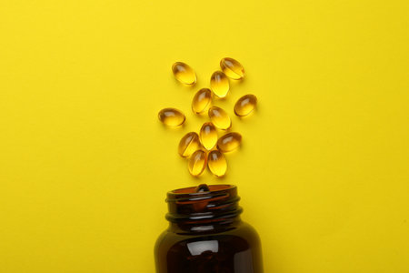 Overturned bottle with dietary supplement capsules on yellow background, flat layの写真素材