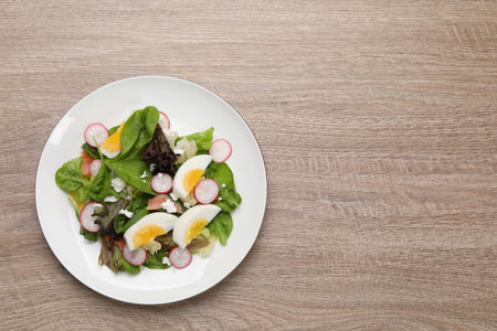 Delicious salad with boiled egg, radish and cheese on wooden table, top view. Space for text