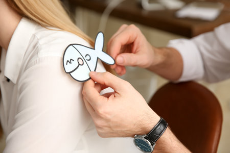Man sticking paper fish to colleague's back in office, closeup. funny joke