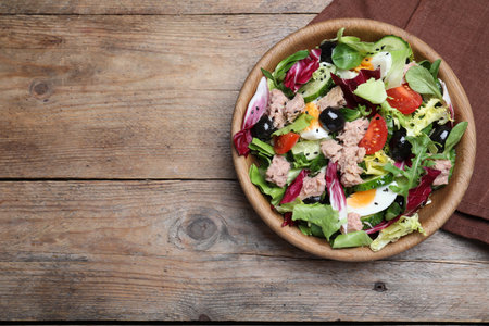 Bowl of delicious salad with canned tuna and vegetables on wooden table, flat lay. Space for textの写真素材