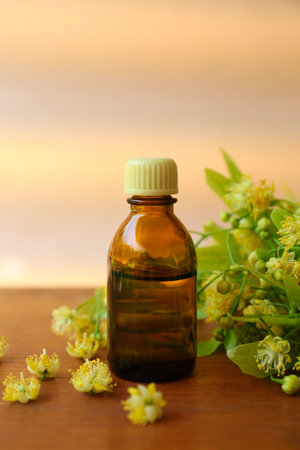 Bottle of essential oil and linden blossoms on wooden table against blurred backgroundの写真素材