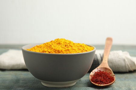 Bowl of saffron powder and spoon with dried flower stigmas on light blue wooden tableの写真素材