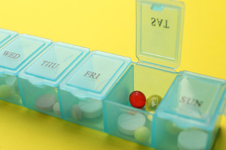 Plastic box with different pills on yellow background, closeupの写真素材