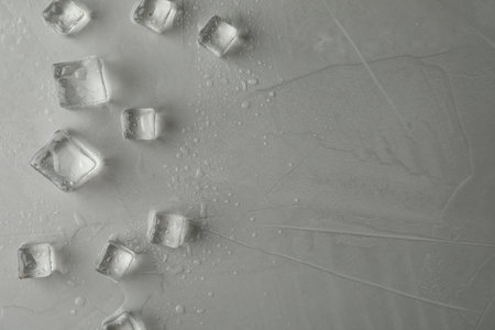 Crystal clear ice cubes with water drops on gray table, flat lay. Space for text