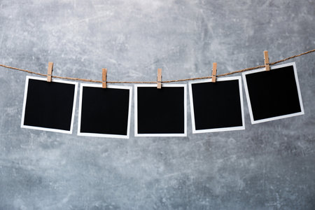 Wooden clothespins with empty instant frames on twine against gray background. Space for text