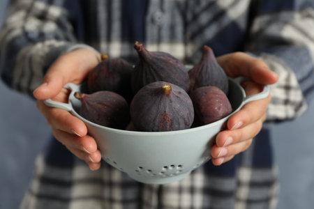 Woman holding colander with tasty raw figs on light blue background, closeupの写真素材