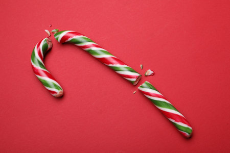 Broken sweet Christmas candy cane on red background, top view