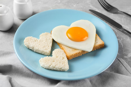 Romantic breakfast with heart shaped fried egg and toasts served on gray marble table