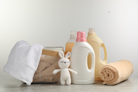 Bottles of laundry detergents, fresh towels, knitted rabbit toy on gray table against white backgroundの写真素材