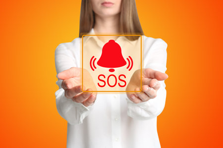 Young woman holding virtual icon SOS on orange background, closeupの写真素材