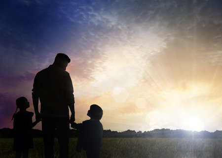 Silhouettes of godparent with children in field at sunriseの写真素材