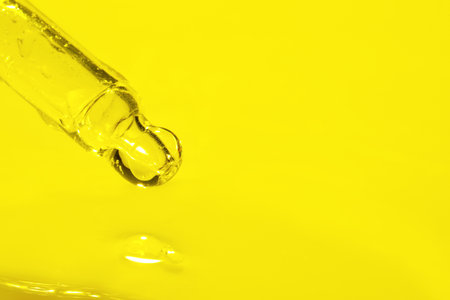 Dripping face serum from pipette on yellow background, closeup. Space for textの写真素材