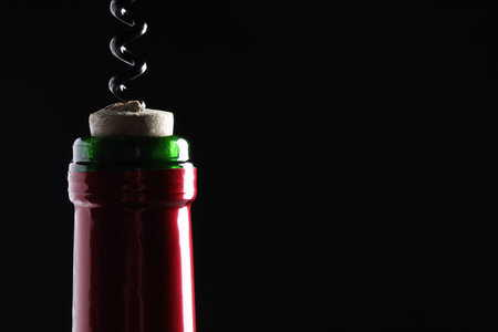 Opening wine bottle with corkscrew on dark background, closeup. Space for textの写真素材