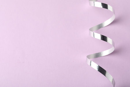 Shiny serpentine streamer on lilac background, top view. Space for textの写真素材