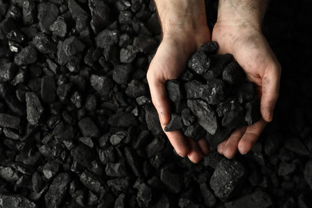 Man holding coal in hands over pile, top view. Space for textの写真素材