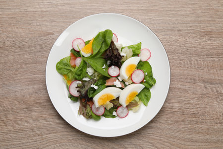 Delicious salad with boiled egg, radish and cheese on wooden table, top viewの写真素材