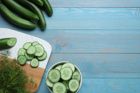 Fresh ripe cucumbers and dill on light blue wooden table, flat lay. Space for textの写真素材