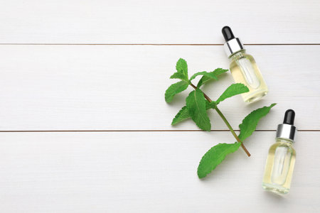 Bottles of essential oil and mint on white wooden table, flat lay. Space for textの写真素材