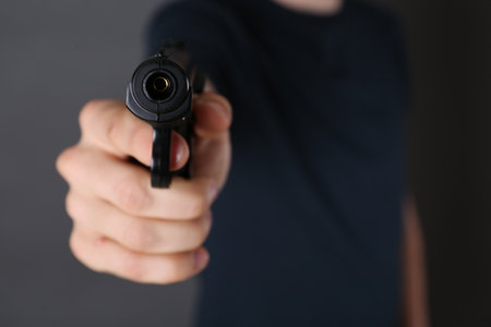 Man aiming gun on dark background, closeup