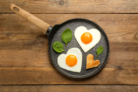 Heart shaped fried eggs with toast in frying pan on wooden table, top viewの写真素材