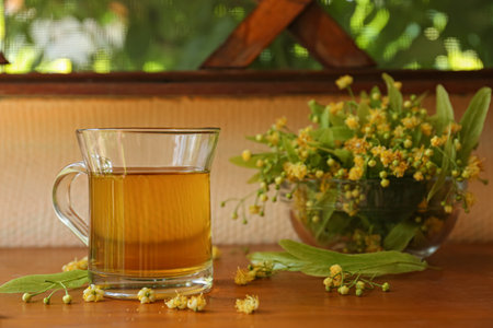 Glass cup of aromatic tea and linden blossoms on wooden table, space for textの写真素材