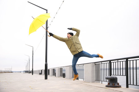 Man with yellow umbrella caught in the thick of wind outdoorsの写真素材