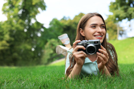 Young woman with camera on green grass outdoors, space for text. interesting hobby