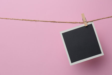 Wooden clothespin with empty instant frame on twine against pink background. Space for text