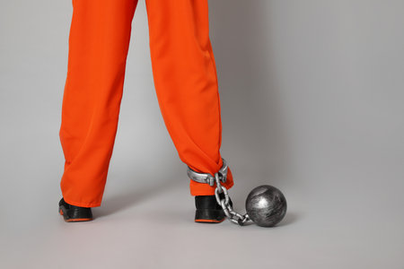Prisoner in orange jumpsuit with metal ball on gray background, closeup. Space for textの写真素材
