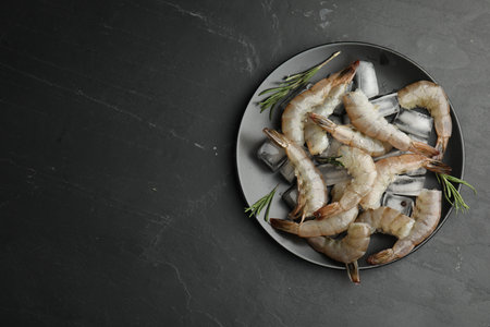 Fresh raw shrimps with rosemary and ice cubes on black table, top view. Space for textの写真素材