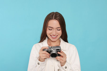 Young woman with camera on light blue background. interesting hobby