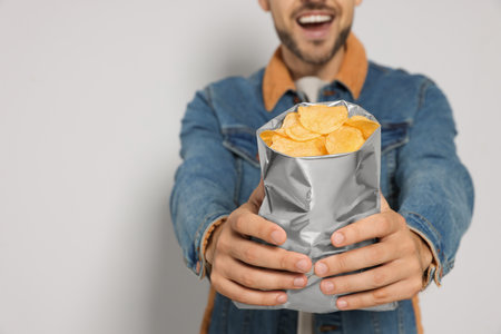 Handsome man with potato chips against light gray background, closeup. Space for textの写真素材