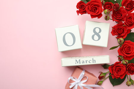 Wooden block calendar with date 8th of March, gift and roses on pink background, flat lay. Space for...
