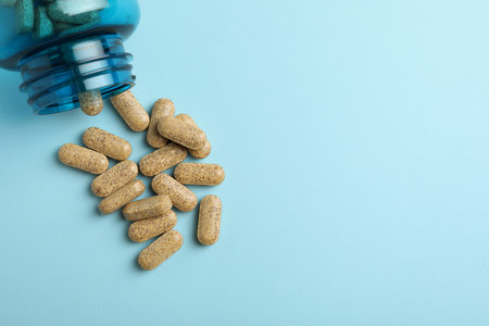 Overturned bottle with dietary supplement pills on light blue background, flat lay. Space for textの写真素材