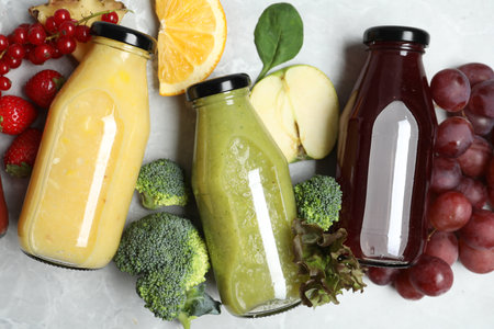 Bottles of delicious juices and fresh fruits on marble table, flat layの写真素材