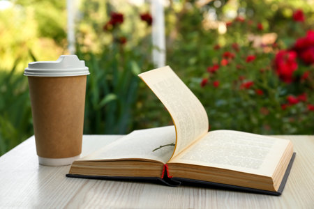 Open book with paper cup of coffee on wooden table in gardenの写真素材