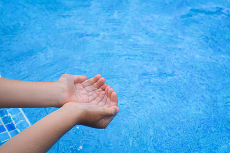 Girl holding water in hands above pool, closeupの写真素材