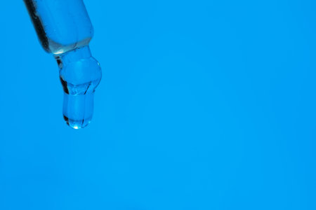 Dripping face serum from pipette on blue background, closeup. Space for textの写真素材