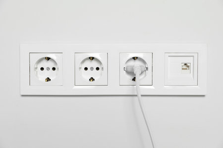 Power sockets with inserted plug on white wall. electrical supplyの写真素材
