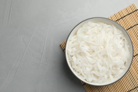 Bowl with cooked rice noodles and straw mat on light gray table, top view. Space for textの写真素材